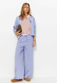 Ensemble de vêtements de détente avec des rayures verticales bleues et blanches. Comprend une chemise à boutons, un pantalon à cordon de serrage et un haut rose clair. Sabots en suède brun.