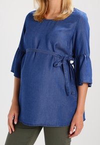 Jeanstopp för gravida med utställda ärmar, knyt i midjan och rundad halsringning i en mellanblå nyans. Mjuk textur och avslappnad passform.