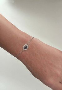 Hopeakorumus, jossa on oktogonaalinen musta jalokivi keskipisteenä, ympärillä pieniä kirkaita kiviä, esillä ranteessa.