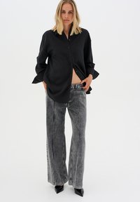 Black button-up shirt with long sleeves, worn over gray flared jeans with a faded texture and white stitching; black pointed heels complete the outfit.