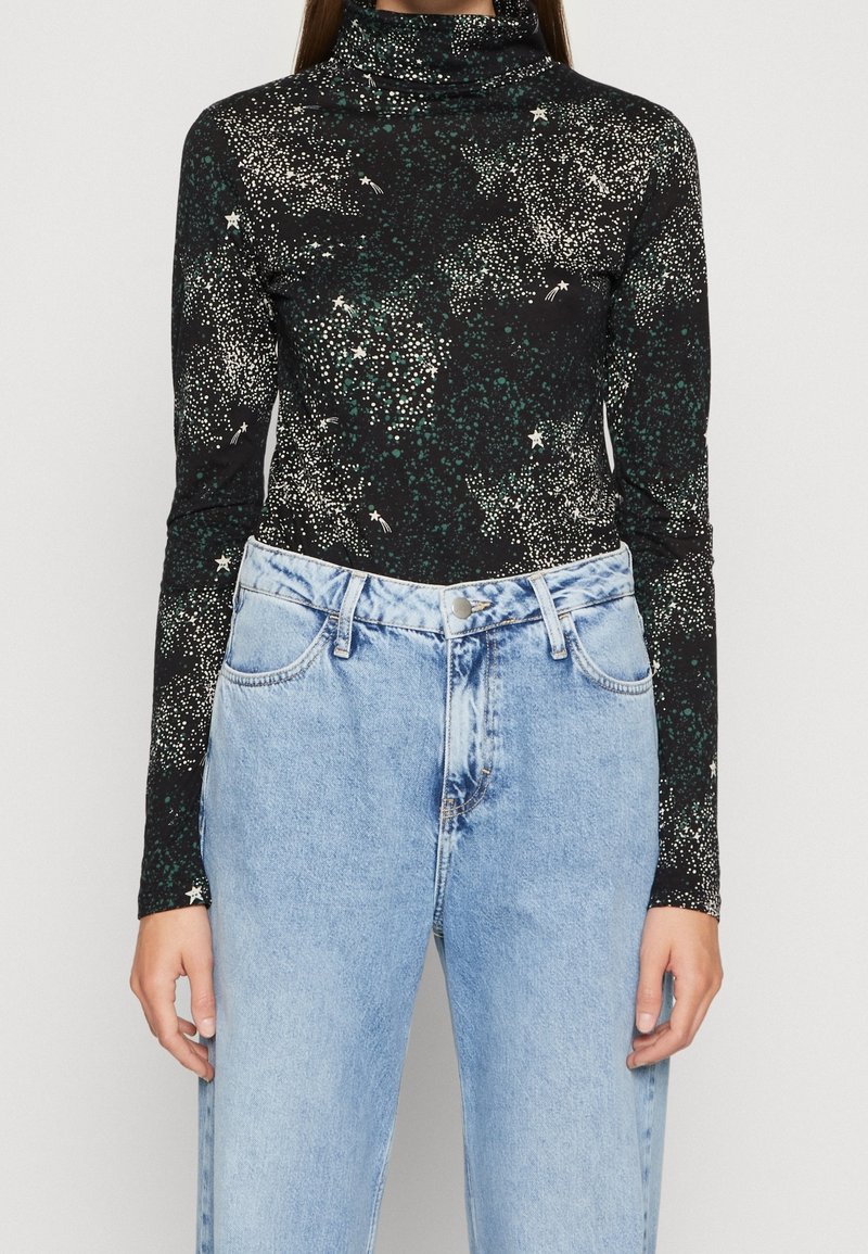 Svart långärmad polotröja med ett stjärnmönster, som har vita och gröna prickar. Kombineras med ljusblå högmidjade jeans.