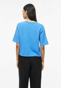 T-shirt bleu court en tissu doux, avec des manches courtes et un col rond. Le dos est simple avec peu de détails.