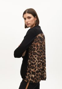 Černé tričko s dlouhými rukávy a skládacím zadním dílem v leopardím vzoru. Měkká textura, ležérní design, zaoblený lem a jemné detaily límce.