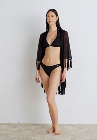 Melnā bikini komplekts, ko papildina caurspīdīgs melns kimono ar frēzētām malām, izceļot minimālistisku dizainu un vieglu tekstūru.