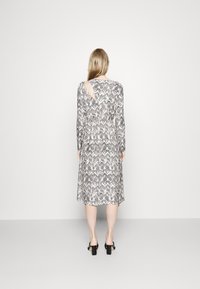 Dlouhé rukávy šaty s černobílým vzorem, ke kolenům, s výřezem vzadu a přiléhavým pasem. Hladká textura.