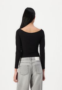 Black long-sleeve top with a scoop back, made of smooth fabric. Paired with high-waisted, light grey jeans featuring back pockets.