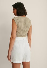 Beige strikket ærmeløs top med et struktureret ribmønster, parret med hvide linnedshorts med rullet kant og skræddersyet pasform.