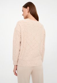 Maglione a maglia rosa chiaro con un motivo testurizzato, caratterizzato da sottili specks dorati e orlo a costine. La parte posteriore è semplice con un collo rotondo.