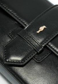 Czarna skórzana torebka o błyszczącym wykończeniu, z haftowaną rączką i złotym emblematem ptaka jako wyróżniającym się detalem.