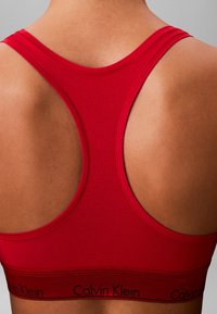 Rotes Sport-BH aus glattem Stoff mit Racerback-Design. Verfügt über das schwarze Calvin Klein-Logo auf dem elastischen Bündchen unten.