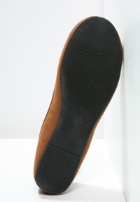 Rudos suede pusiau batai su glotniu viršumi, plokščiu juodu guminiu padu, turinčiu tekstūrinį sukibimo raštą, ir apvaliu logotipo įspaudu šalia kulno.