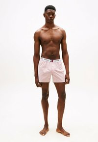 Boxer in cotone a righe rosse e bianche con cintura elastica, caratterizzati dal nome del marchio "TOMMY HILFIGER" stampato in nero.