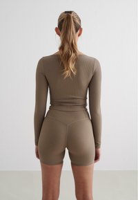 Ensemble composé d'un haut à manches longues en tissu côtelé et de shorts, dans une teinte brune douce, avec un design ajusté et une texture douce. Détails de couture au niveau de la taille.