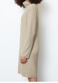 Robe-pull beige côtelée avec un col montant, des manches longues et une coupe décontractée, confectionnée dans un matériau en maille douce.