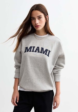 Grå sweatshirt med "MIAMI" tryckt i marinblått, med rund hals och långa ärmar. Tyget verkar mjukt och avslappnat.