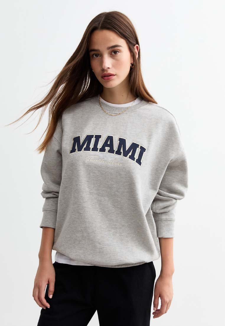 Felpa grigia con la scritta "MIAMI" stampata in blu navy, caratterizzata da un collo tondo e maniche lunghe. Il tessuto sembra morbido e informale.