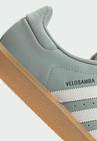 Vaaleanvihreät lenkkarit, joissa on teksturoitu nahka päällinen, valkoiset raidat ja kumipohja. Materiaalit sisältävät sileän ja nahan kaltaisen pinnan.