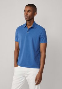 Polo azul hecho de algodón, con un collar clásico, dos botones en el cuello y mangas cortas, combinado con pantalones blancos.