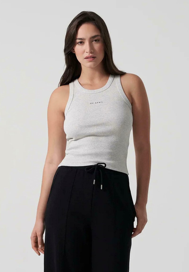 Hallgrimud rihmaga tank top, millel on ümmargune kaelus ja logo keskel, koos mustade nööriga pükstega. Sile tekstuur, keha järgiv disain.