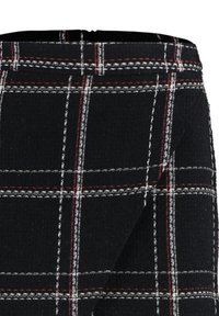 Tissu noir avec un motif à carreaux blancs et rouges, montrant des coutures détaillées et une partie d'une ceinture.