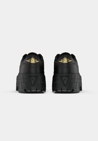 Czarne, masywne sneakersy Air Jordan widokiem z tyłu, wyposażone w złote logo skrzydła Air Jordan oraz grube, fakturowane podeszwy.