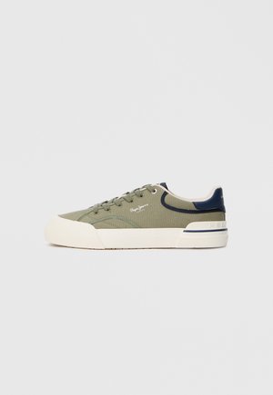 Green canvas sneakers with beige rubber soles, navy accents, and round laces. Features logo detailing on the side and a textured finish.