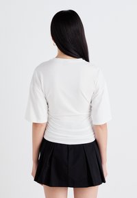 Witte top met korte mouwen en gerimpelde details op de rug, gecombineerd met een zwarte geplooide mini-jurk. Gladde stof en een relaxte pasvorm.
