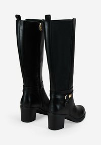 Par de botas de cuero negras hasta la rodilla con tacones de bloque, cremallera lateral, paneles elásticos y detalle de correa con hebilla alrededor del tobillo.