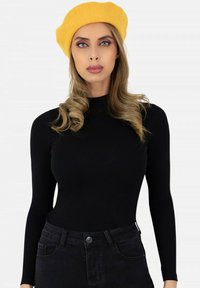 Haut noir à manches longues avec un col haut, associé à un jean noir taille haute, complété par un béret jaune vif. Texture lisse.