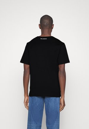 Mann trägt schwarzes Karl Lagerfeld T-Shirt und blaue Jeans, von hinten vor weißem Hintergrund gezeigt.
