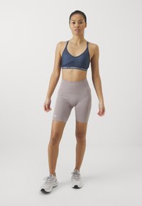 Sujetador deportivo azul marino con tirantes finos, combinado con pantalones cortos de compresión de cintura alta en gris claro, que presentan el logo de Under Armour en la banda de la cintura.