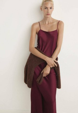 Vestido de satén burdeos con tirantes finos, combinado con un cárdigan de punto texturizado en marrón. La tela cae suavemente, creando una silueta elegante.