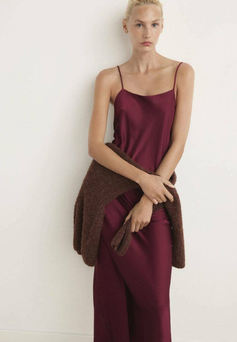 Vestido de satén burdeos con tirantes finos, combinado con un cárdigan de punto texturizado en marrón. La tela cae suavemente, creando una silueta elegante.