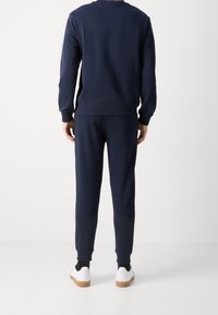 Felpa blu navy e pantaloni abbinati in morbido cotone misto. La felpa presenta polsini a costine, i pantaloni hanno una vita elastica e tasche laterali.