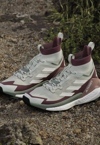 Vaaleanharmaat ja burgundinväriset urheilukengät, joissa on korkea nilkkadesign, teksturoitu päällinen, valkoiset raidat ja kumipohja pitoon.