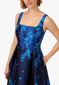 Blaues, mit Blumen besticktes Kleid mit eckigem Ausschnitt und breiten Trägern, gefertigt aus einem glatten, dunkelblauen Stoff mit leichtem Glanz.