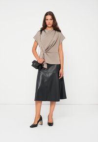 Blusa beige con dettaglio annodato sul davanti, abbinata a una gonna midi in pelle nera, scarpe nere con tacco a blocco e una borsa a tracolla piccola.