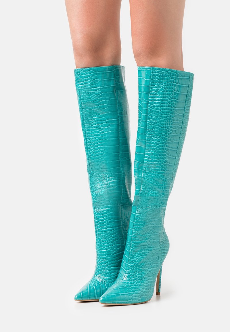 Botas turquesas hasta la rodilla, en piel brillante con estampado de cocodrilo en relieve, con punteras puntiagudas y altos tacones de aguja.