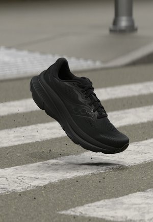 Μαύρο αθλητικό παπούτσι που τρέχει στον αέρα πάνω από διάβαση πεζών σε ασφαλτοστρωμένο δρόμο, με μικρά υπολείμματα να πετάγονται από κάτω του.