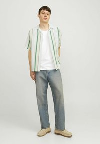 Camicetta a maniche corte con strisce verdi e bianche, abbinata a una maglietta bianca e jeans a gamba dritta di un blu chiaro, completata da calzature beige.