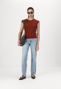Rustfarget tettsittende topp, lyseblå jeans med frynsete kant, svarte slingback-flats og en grå skulderveske. Minimalistiske solbriller fullfører looken.