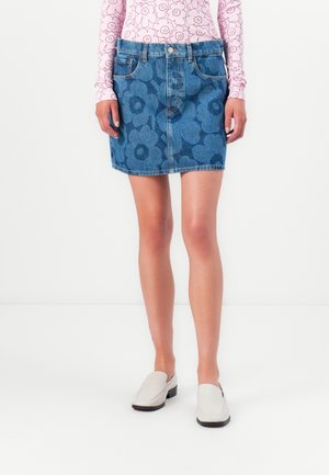 Denim mini skirt with a blue floral pattern, five pockets, and a front button closure. Worn with casual light gray slip-on shoes.
