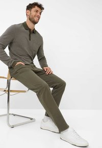 Polo grigio a maniche lunghe con colletto verde e taschino sul petto, abbinato a pantaloni verde oliva e sneakers bianche.