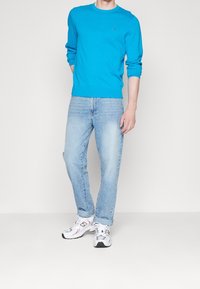 Pull turquoise à manches longues, jean bleu clair et baskets grises avec des touches rouges. Coupe moderne, design décontracté et tissu léger.