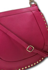 Roze leren tas met een gestructureerde afwerking, voorzien van gouden studs langs de rand en een dunne, verstelbare band. Ritssluiting aan de bovenkant.