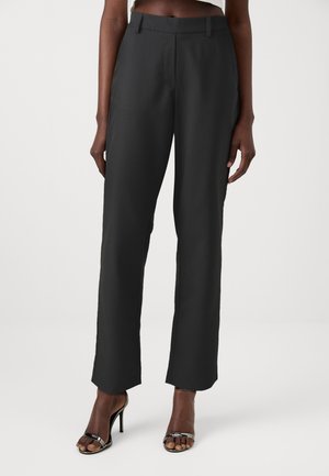 Black tailored trousers with a straight leg design, flat front, and subtle sheen. Worn with black heeled sandals, showcasing a sleek appearance.