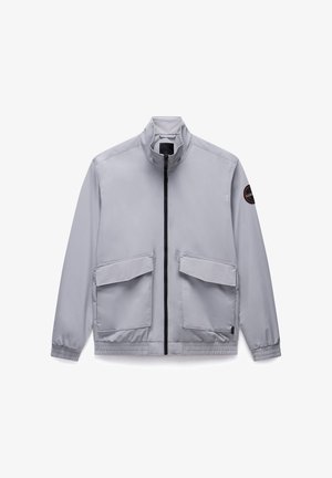 Lys grå zip-up jakke med høj krave, to forlommer, elastiske manchetter og et logo patch på venstre ærme. Glat, letvægtigt stof.