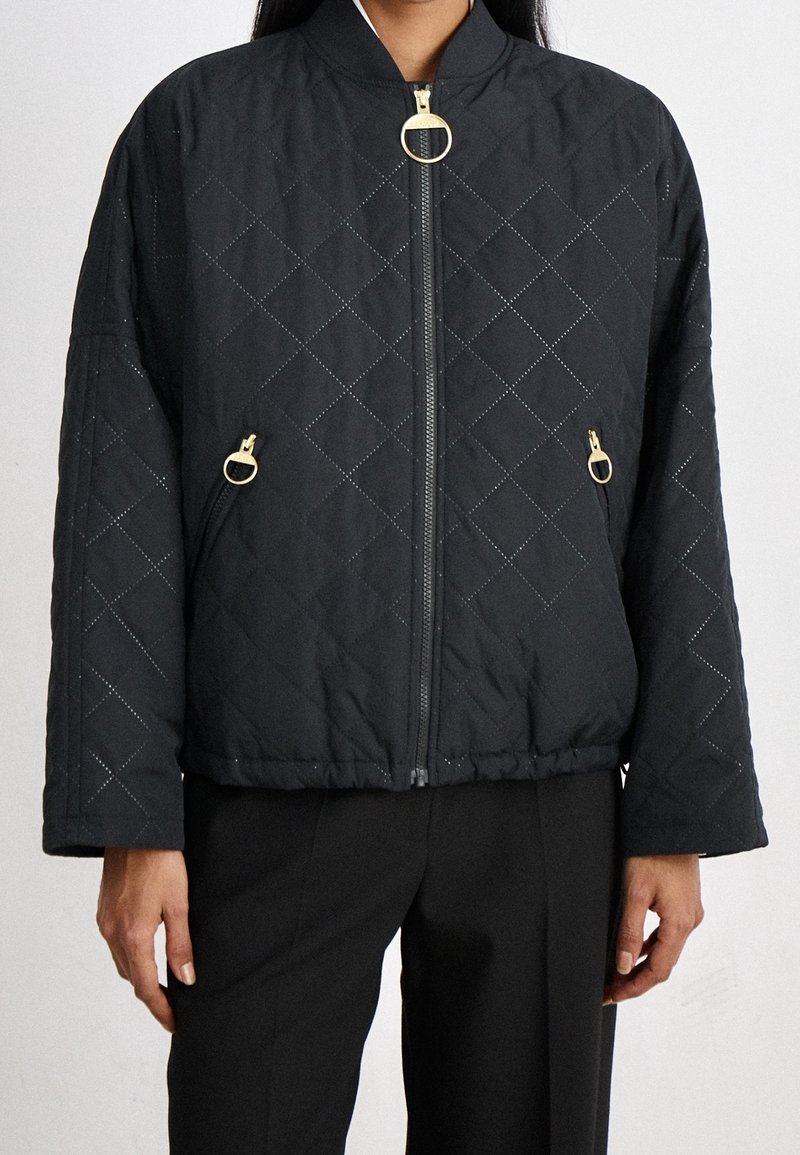 Black quilted jacket with diamond pattern, ribbed hem, and gold hardware accents, featuring a front zipper and side pockets.