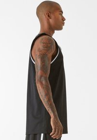 Melna bez piedurknēm krūšturis ar apaļu kakla izgriezumu, ar baltiem akcentu svītrainiem plecos un teksturētu, elpojošu audumu.