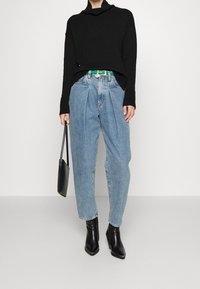 Black knitted sweater with a cowl neck, light blue high-waisted jeans, green belt, black pointed ankle boots, and a small black handbag.